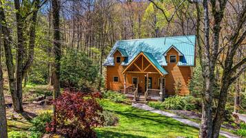 A log cabin with a green roof, surrounded by a forest.