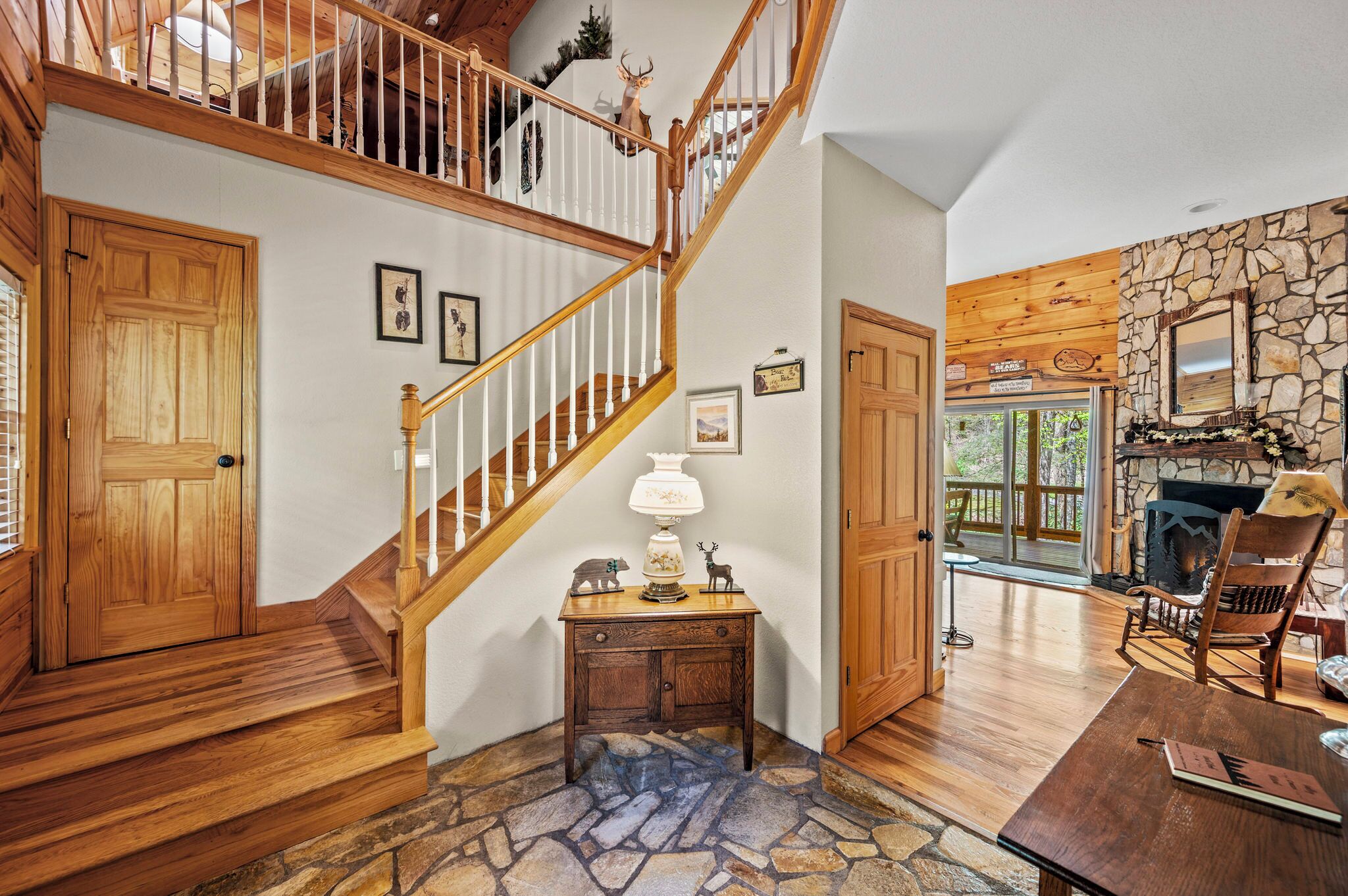 A wooden staircase leading to a second floor, a stone fireplace, and a wooden dining table with a lamp.