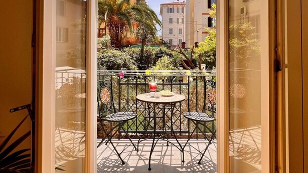An open door leading to a balcony with a table and chairs, surrounded by greenery and buildings in the background. - New apartment in the city center cozy and quiet near the station (La Spezia)