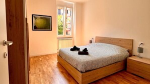 A bedroom with a wooden bed, a nightstand, and a window with a view of greenery. - New apartment in the city center cozy and quiet near the station (La Spezia)