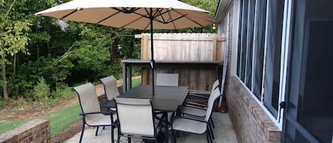 An outdoor patio with a table and chairs, a large umbrella, and a wooden fence in the background.