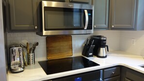 A kitchen with a microwave, toaster, coffee maker, and a wooden cutting board.