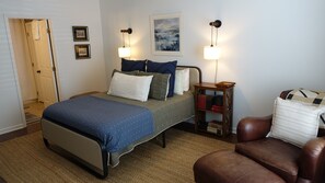 A bedroom with a bed, bedside table, lamp, and a chair.