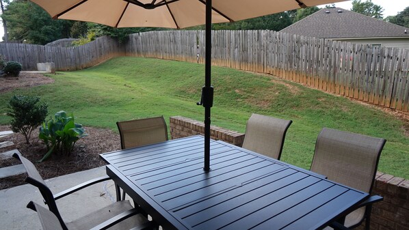 An outdoor patio with a table and chairs, a wooden fence in the background, and a small garden area.