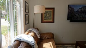 Een woonkamer met een bruine leren bank, een lamp, ingelijste foto’s en een schilderij aan de muur.