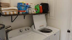 A laundry area with a Whirlpool washer and dryer, a shelf with laundry supplies, and a door.