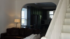 Un salon avec un canapé, une lampe et un ventilateur de plafond. Un escalier mène à une autre pièce.