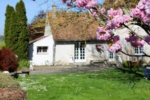 A white house with a red roof, surrounded by a green lawn and flowering trees. - Le Relais D'eugénie : Gîte en Forêt D'orléans (Courcy-aux-Loges)