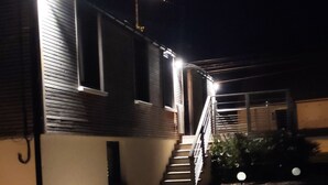 Vue nocturne d’un bâtiment avec un escalier menant au deuxième étage, éclairé par des lampes extérieures.