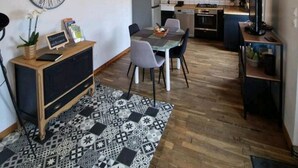 Une cuisine moderne avec un coin repas, agrémentée d’une horloge, de luminaires suspendus et d’un tapis à motifs.