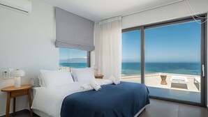 Ein modernes Hotelzimmer mit einem großen Bett, Meerblick und einem Balkon mit Sitzgelegenheit.