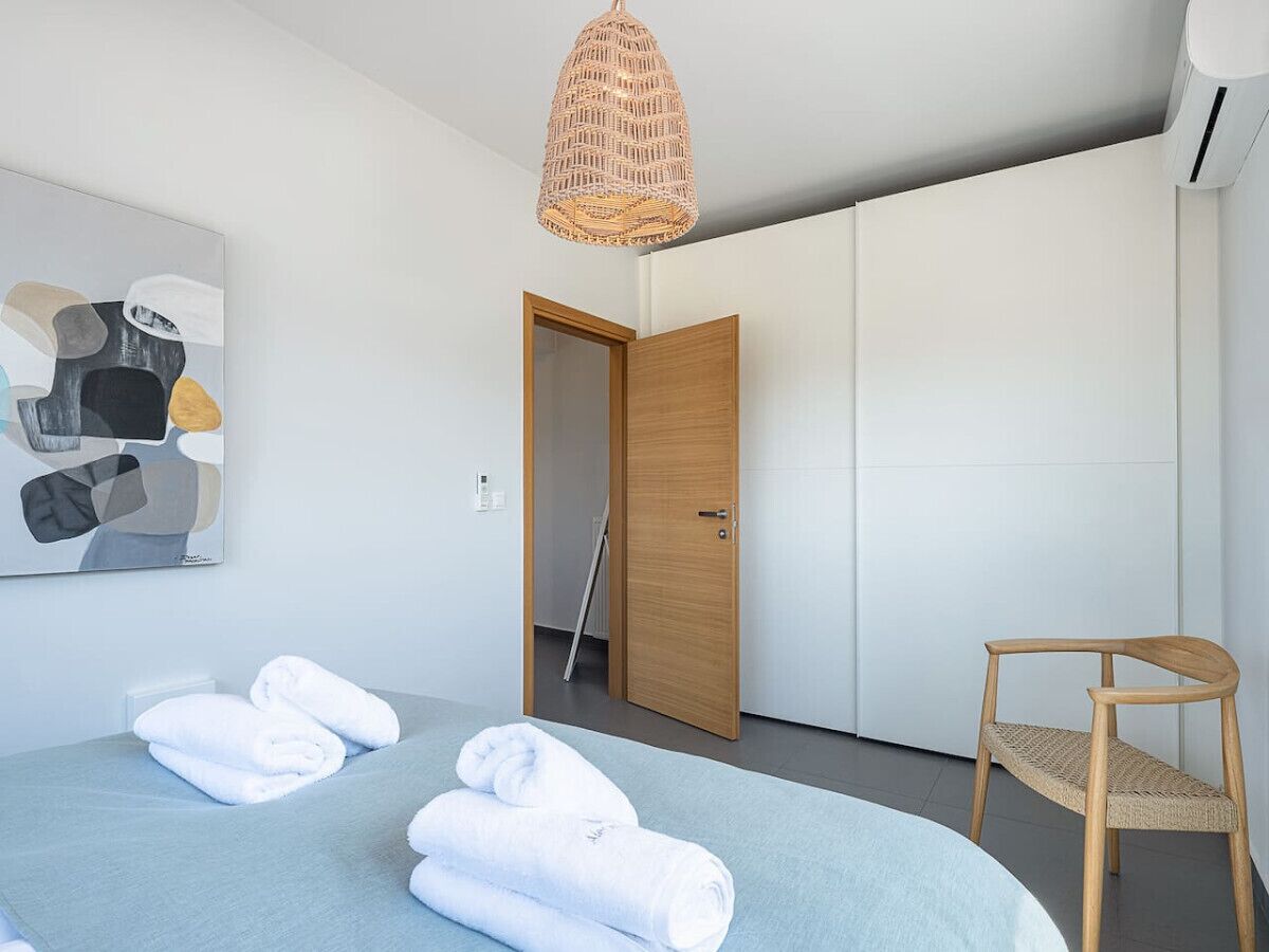 A modern hotel room with a bed, a chair, a door leading to a bathroom, and a wall-mounted artwork.