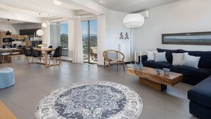 Ein modernes Wohnzimmer mit einem großen runden Teppich, einem dunkelblauen Sofa, einem Holztisch und einem Essbereich mit Holztisch und Stühlen.