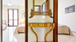 Ein Zimmer mit einem Bett, einem Nachttisch, einem Spiegel und einer Tür zu einem anderen Raum.