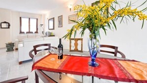 Ein Essbereich mit einem Tisch für zwei Personen, einer Vase mit gelben Blumen und einer Weinflasche.