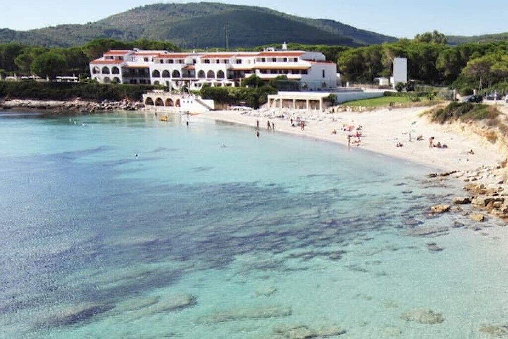 A coastal hotel with a large building, a sandy beach, and clear turquoise waters.