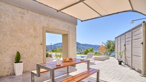 Une terrasse en pierre avec une table et un banc en bois, un pot de fleurs et une vue sur les montagnes.