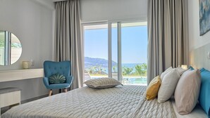 Une chambre avec un grand lit, une chaise bleue, une table de chevet et une vue sur la mer.