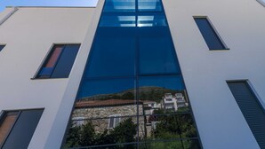 A modern building with large glass windows reflecting a hillside and traditional buildings below. - Rausion Luxury Apartments (Dubrovnik)
