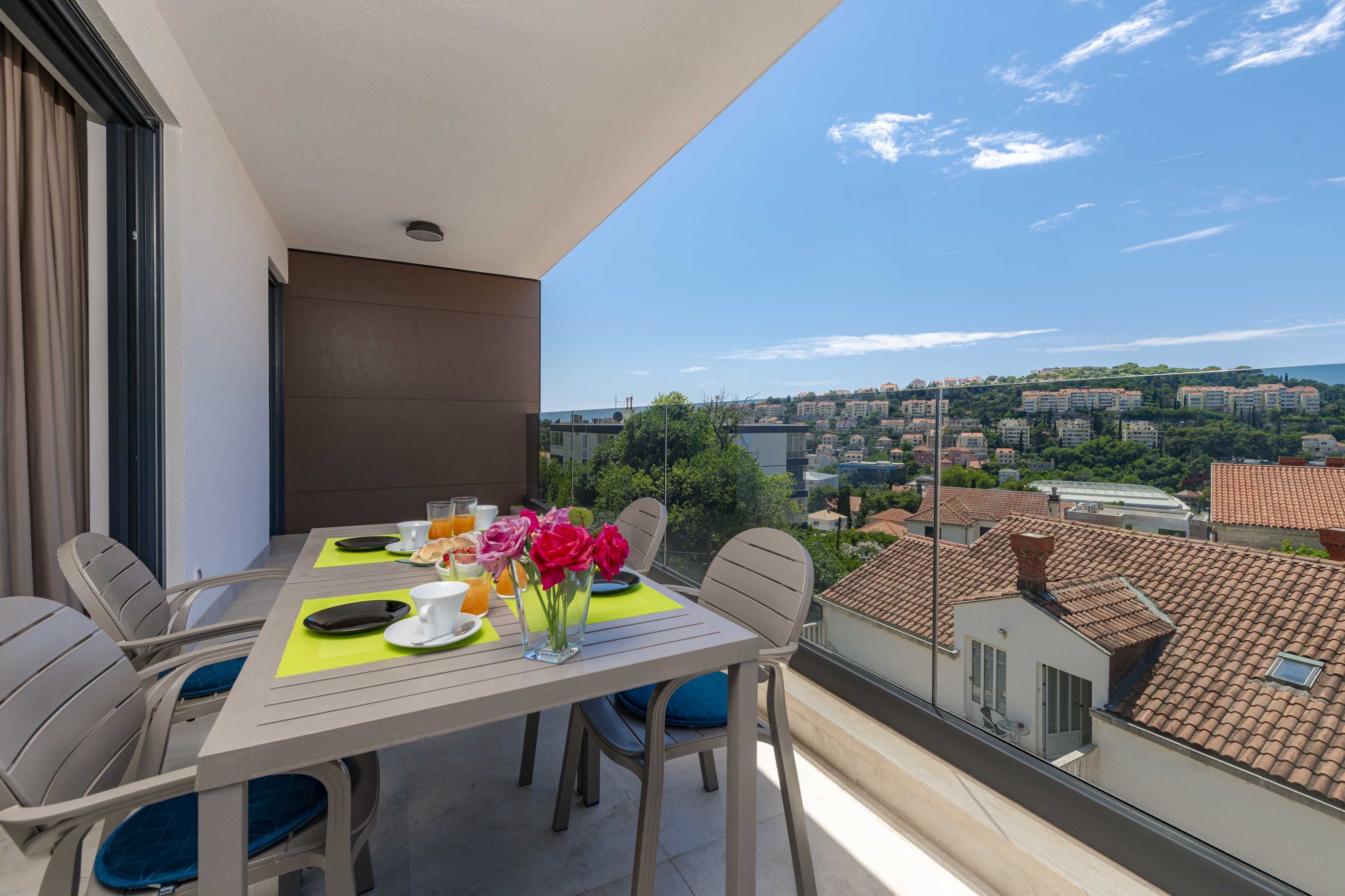 Un balcón con mesa lista para el desayuno, sillas y vista a la ciudad.
