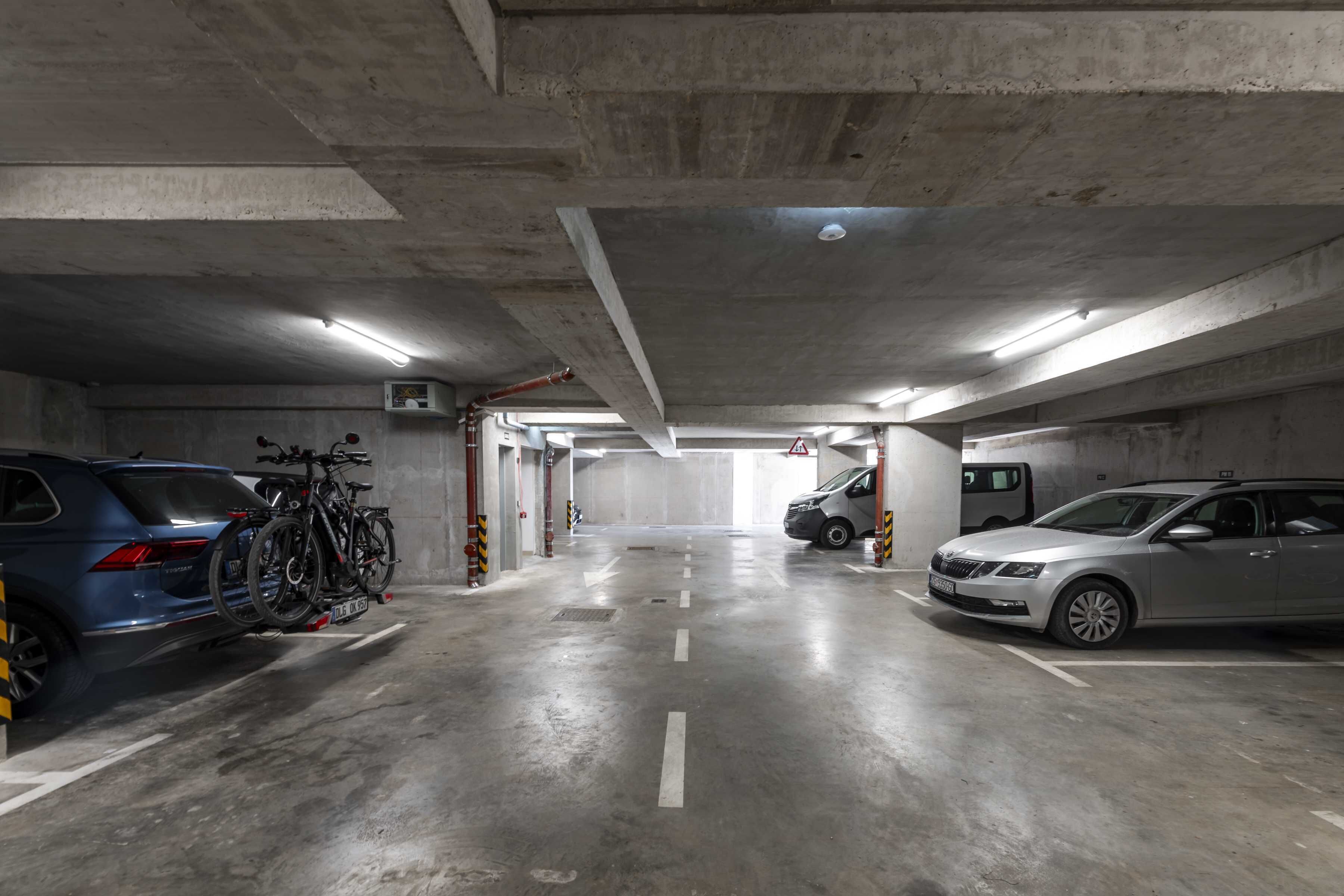 A multi-level parking garage with concrete walls and floors, featuring several parked cars and bicycles.
