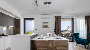 A modern kitchen with a central island, a dining area with two chairs, and a view of the city through a large window. - Rausion Luxury Apartments (Dubrovnik)