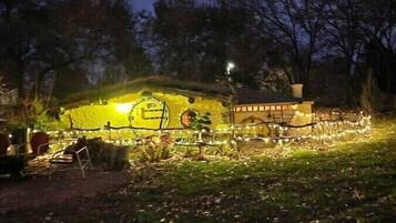 Una casa pequeña e iluminada con puerta y ventanas visibles, rodeada de una valla y árboles.