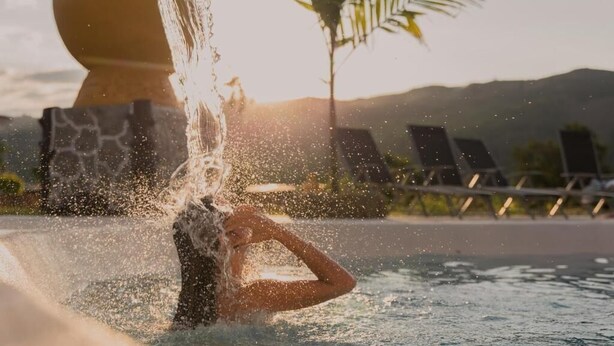 Piscina con agua salpicando, sillas de descanso y una palmera al fondo.