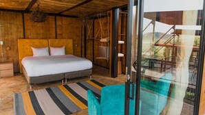 Un dormitorio con techo de madera, una cama con ropa de cama blanca, un tapete a rayas y un ventanal de vidrio que da a un balcón.