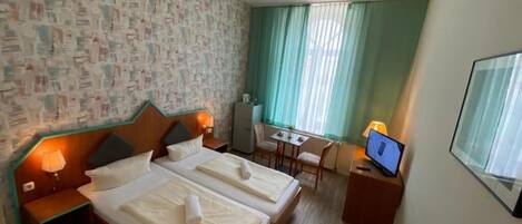 Ein Hotelzimmer mit zwei Betten, einem Schreibtisch, einem Stuhl, einem Fernseher und einem Fenster mit Vorhängen.