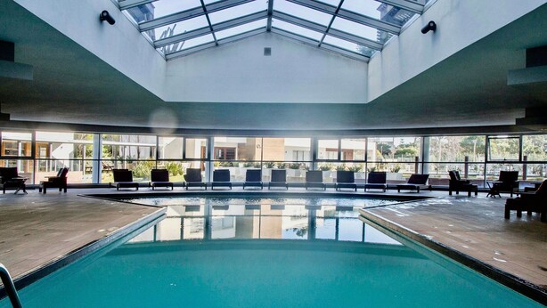 Una piscina interior con tragaluces, sillones de descanso y vistas al exterior.