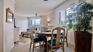 Un comedor con una mesa redonda, sillas, una lámpara y una planta grande en maceta.