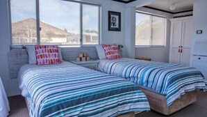 Une chambre avec deux lits, chacun doté de draps à rayures, une fenêtre donnant sur une maison et une armoire blanche.