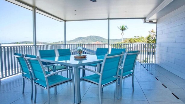 Un espace extérieur abrité, aménagé pour les repas, avec une table et des chaises, offrant une vue sur le paysage et doté d'une rambarde blanche.