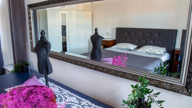 Une chambre avec un grand miroir, un lit avec une literie blanche, une table de chevet et une commode.