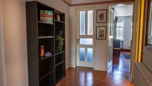 Un couloir avec une bibliothèque noire, une porte blanche dotée de panneaux en verre dépoli et un radiateur sur le côté droit.