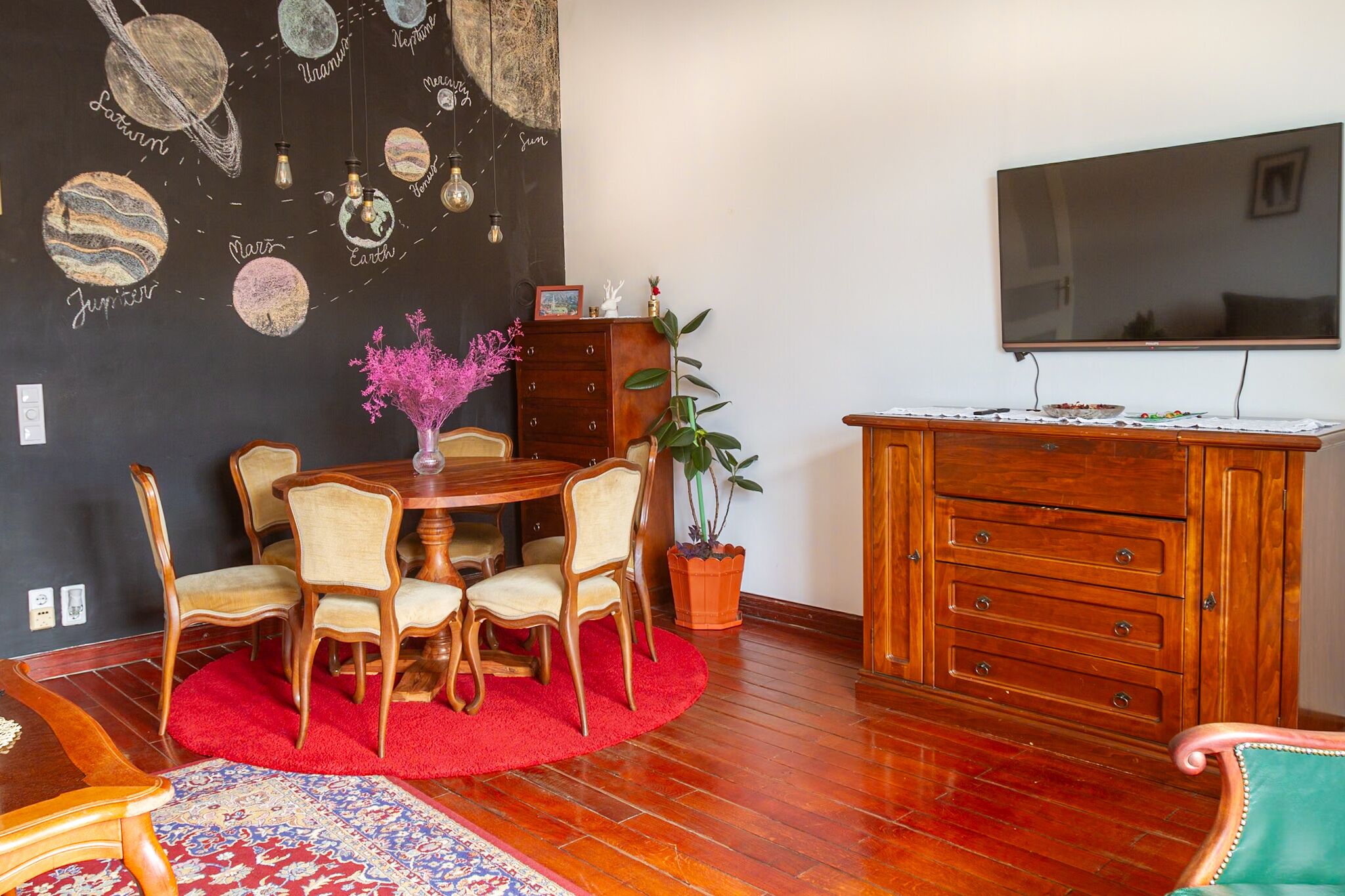 Ein Essbereich mit Holztisch und -stühlen, einem roten Teppich und einem Wandbild mit Planeten.