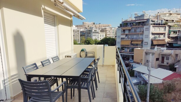 Un balcon avec une table et des chaises, donnant sur un paysage urbain composé de nombreux immeubles.
