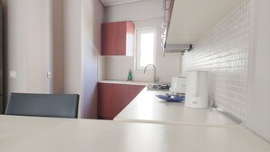Une cuisine avec des plans de travail blancs, un évier et une machine à café. Il y a une fenêtre donnant sur l’extérieur.