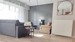 Un salon moderne avec un canapé gris, un fauteuil beige, une petite table ronde et un téléviseur à écran plat, le tout placé devant un mur gris.