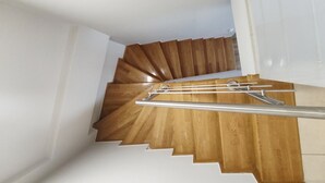 Un escalier en bois avec une rampe métallique, des murs blancs et une porte blanche en haut.
