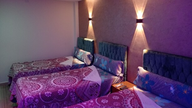 Una habitación con dos camas, cada una con cabecera y varias almohadas. Hay dos lámparas de pared a cada lado de las camas.