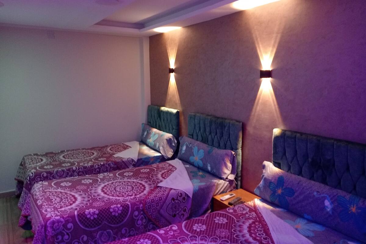 Ein Zimmer mit zwei Betten, jeweils mit Kopfteil und mehreren Kissen. An beiden Seiten der Betten befinden sich jeweils Wandleuchten.