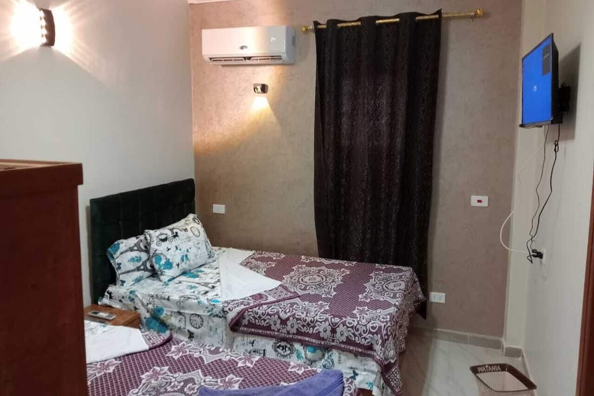 Ein Schlafzimmer mit einem Bett, einer Wandklimaanlage, einem Vorhang und einem an der Wand befestigten Fernseher.