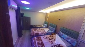 Habitación estrecha con dos camas, cada una con un edredón de estampado diferente. Cuenta con una lámpara en el techo y un aplique de pared.