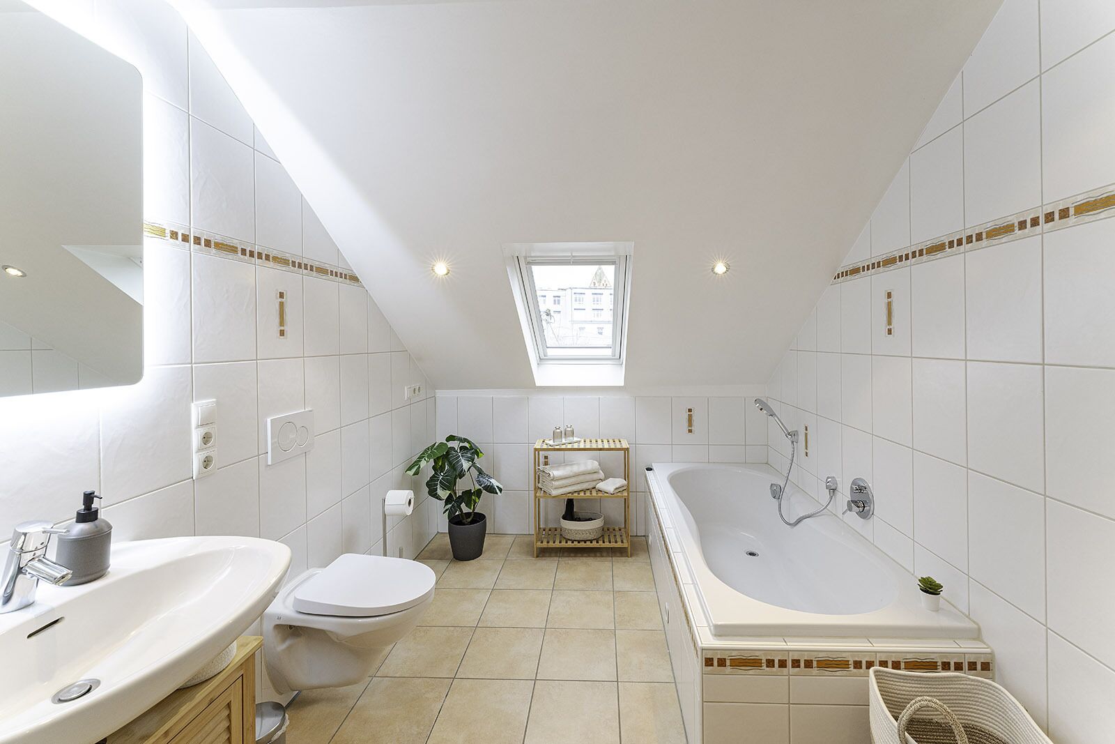 A modern bathroom with a large bathtub, two sinks, a toilet, and a skylight.