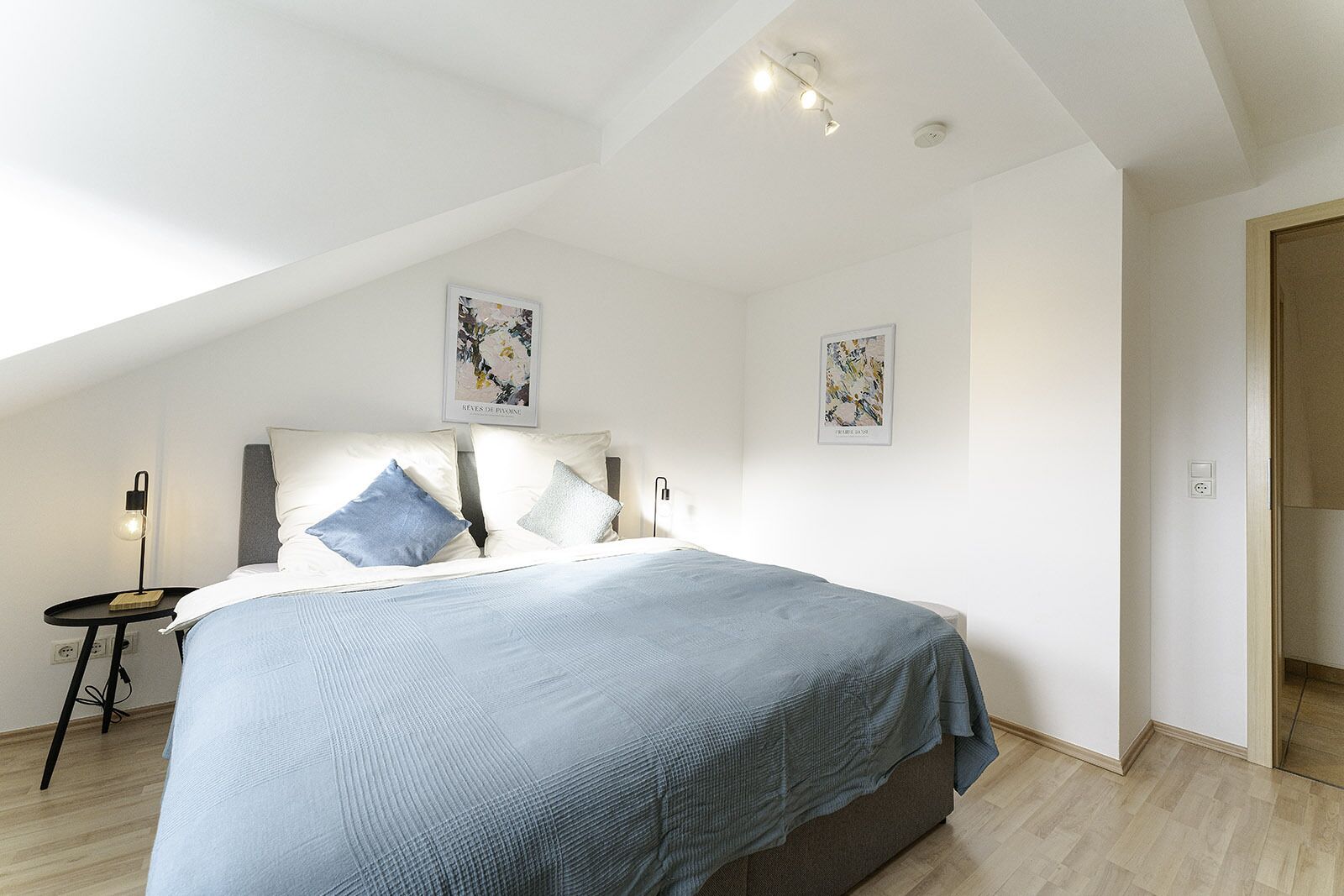 A bedroom with a large bed, a bedside table with a lamp, and two wall-mounted artworks.