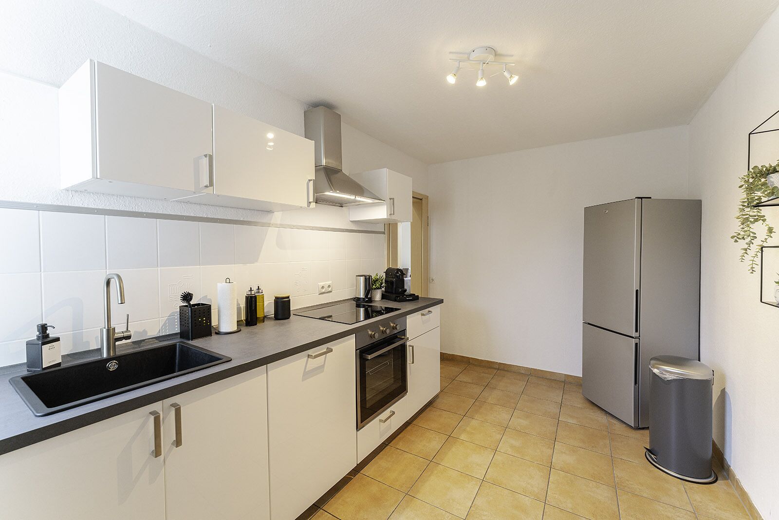 A modern kitchen with white cabinets, a stainless steel refrigerator, and a black countertop.
