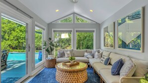 A spacious room with a large window, a comfortable sofa, a round coffee table, and a view of a swimming pool. - 4 Cannon Row at The Sea Pines Resort (Hilton Head Island)