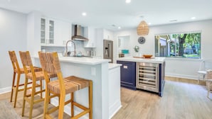 A modern kitchen with white cabinetry, a central island, and a dining area with wooden chairs. - 4 Cannon Row at The Sea Pines Resort (Hilton Head Island)